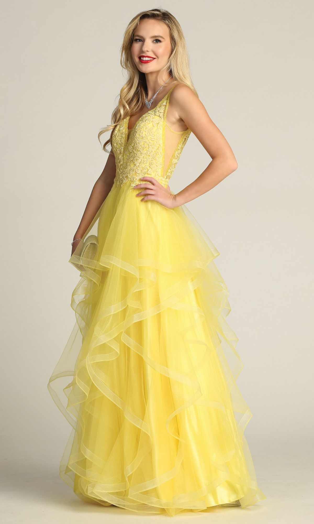 Woman wearing the Chicas XR6006 Sheer-Sides Long Tiered Prom Dress, featuring a beaded v-neck bodice and ruffled a-line skirt, standing against a plain light background.
